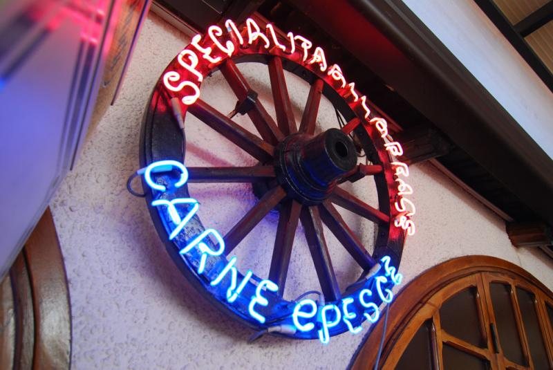 Insegna al neon su ruota di carro: specialità carne e pesce